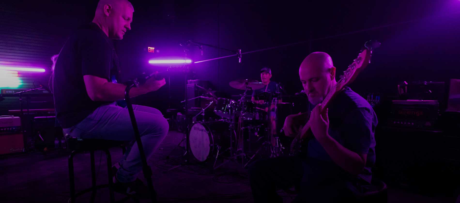 Guitarist, bassist and drummer playing together under purple light