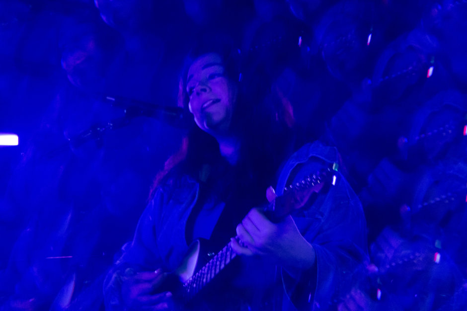 Singer playing electric guitar under blue light, surrounded by prism reflections