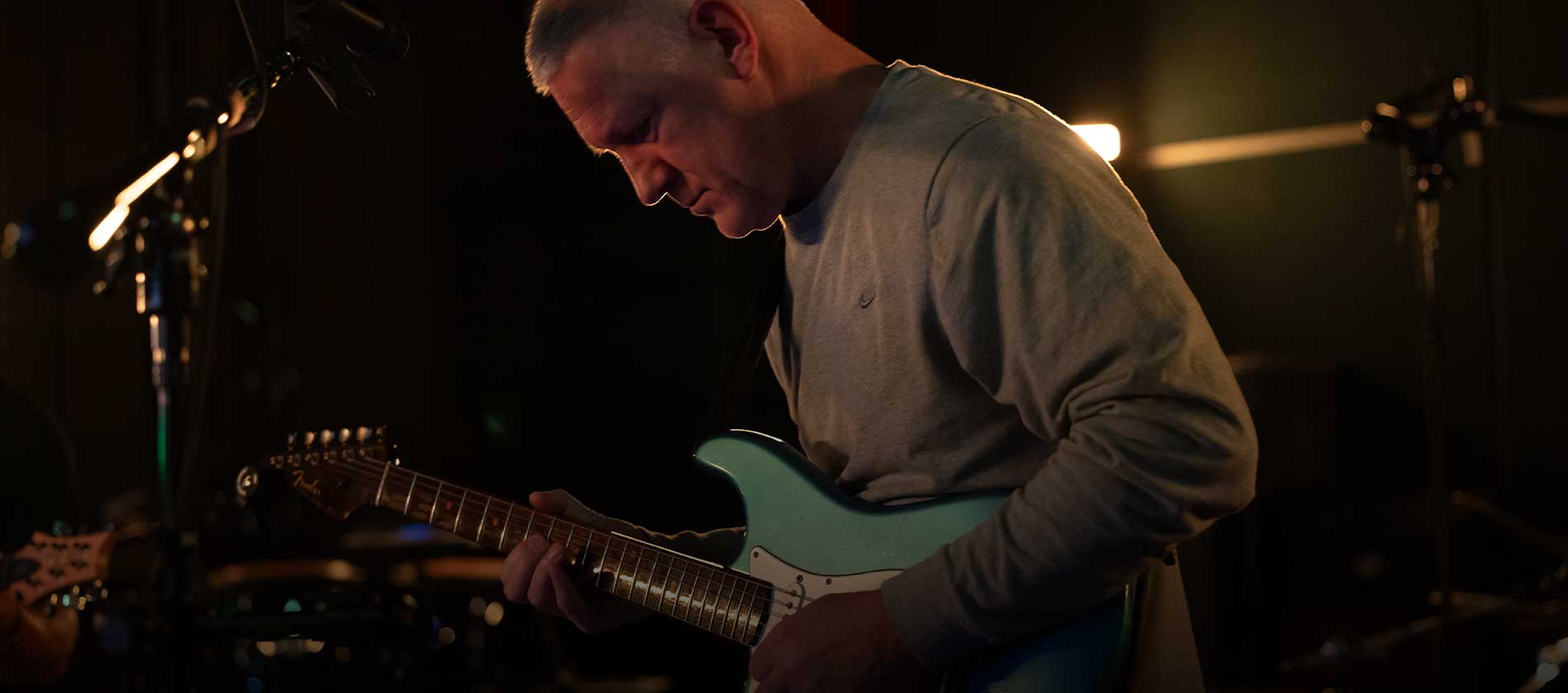 Guitarist in a gray sweater playing electric guitar in the studio