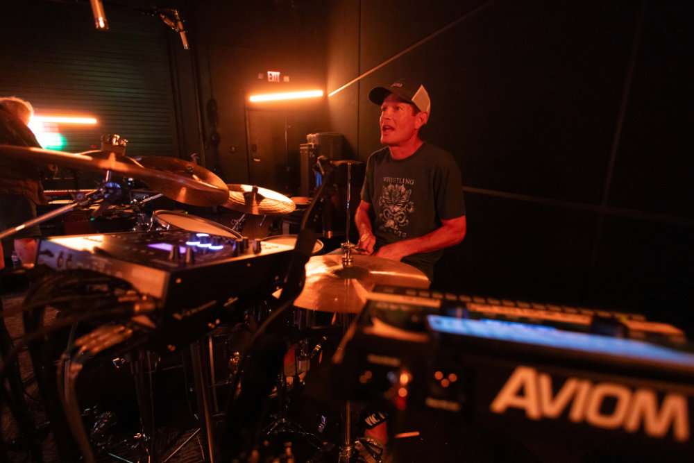Drummer singing along behind his kit in warm studio light
