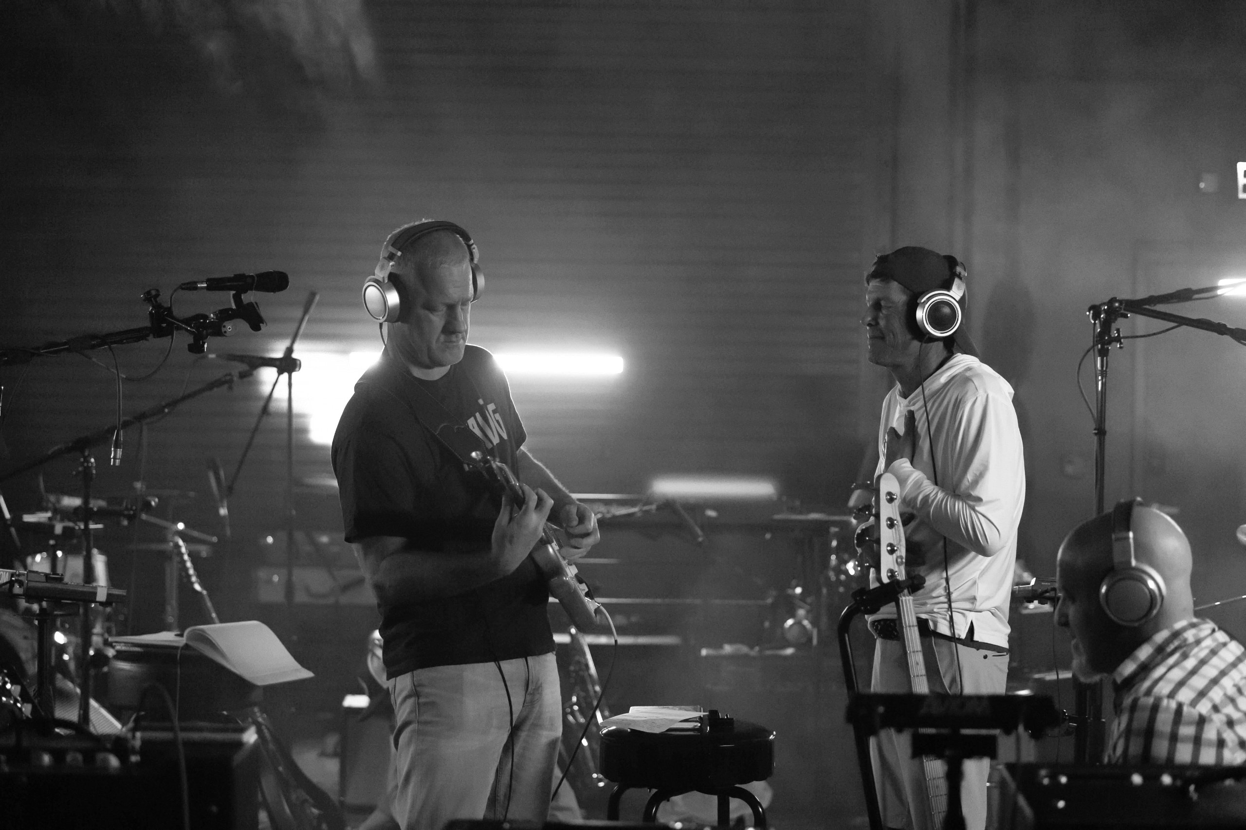 Black-and-white photo of band members in headphones rehearsing in the studio