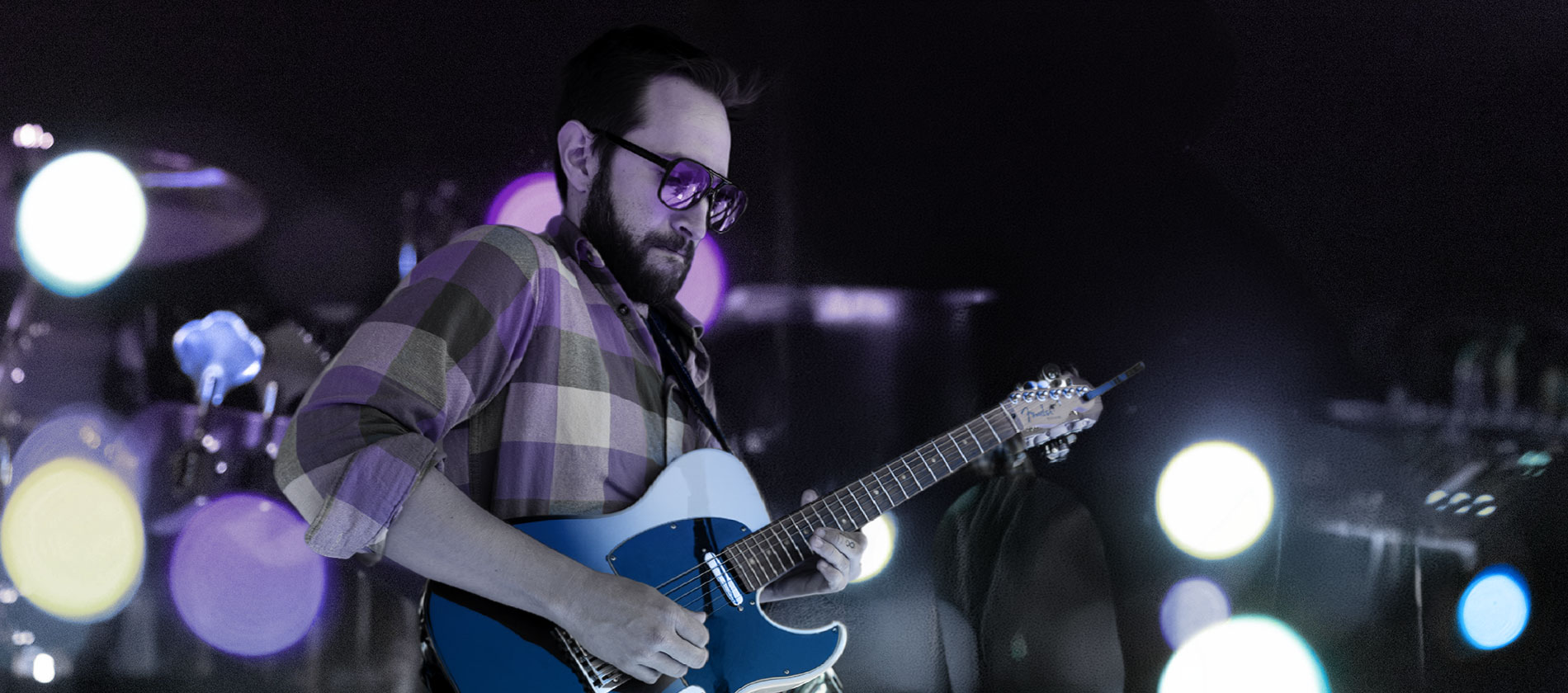 Guitarist in tinted glasses playing a blue electric guitar among glowing lights