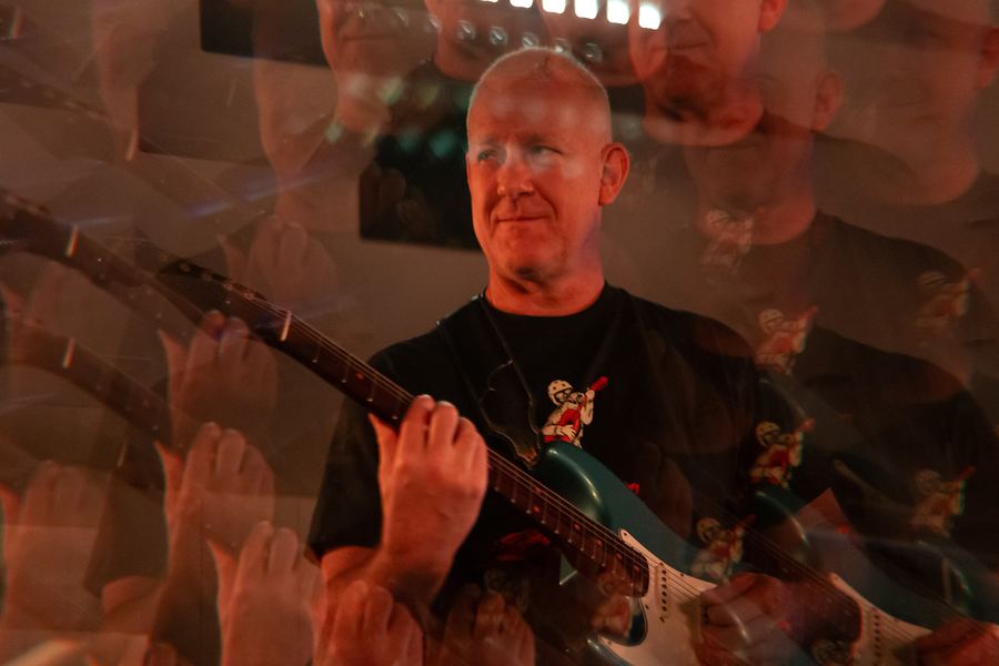 Smiling guitarist playing electric guitar amid prism reflections