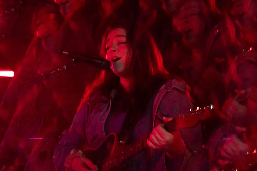 Singer with long hair singing and playing guitar under red light
