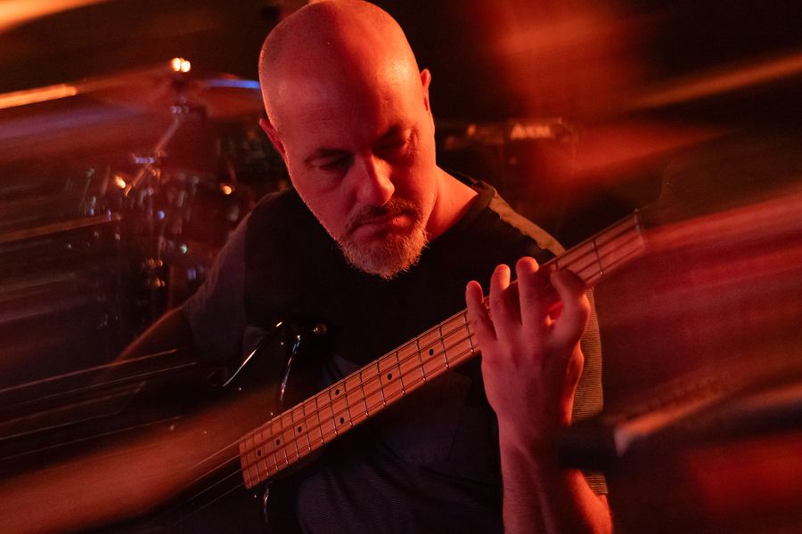 Bassist playing under red light with motion-blur streaks