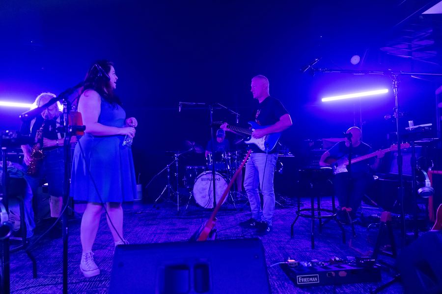 The full band rehearsing under blue and purple lights, a singer in a blue dress at center