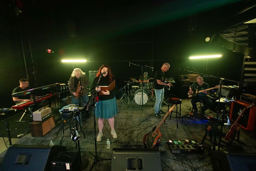 Wide view of the full band rehearsing: keys, saxophone, vocals, drums, guitar and bass