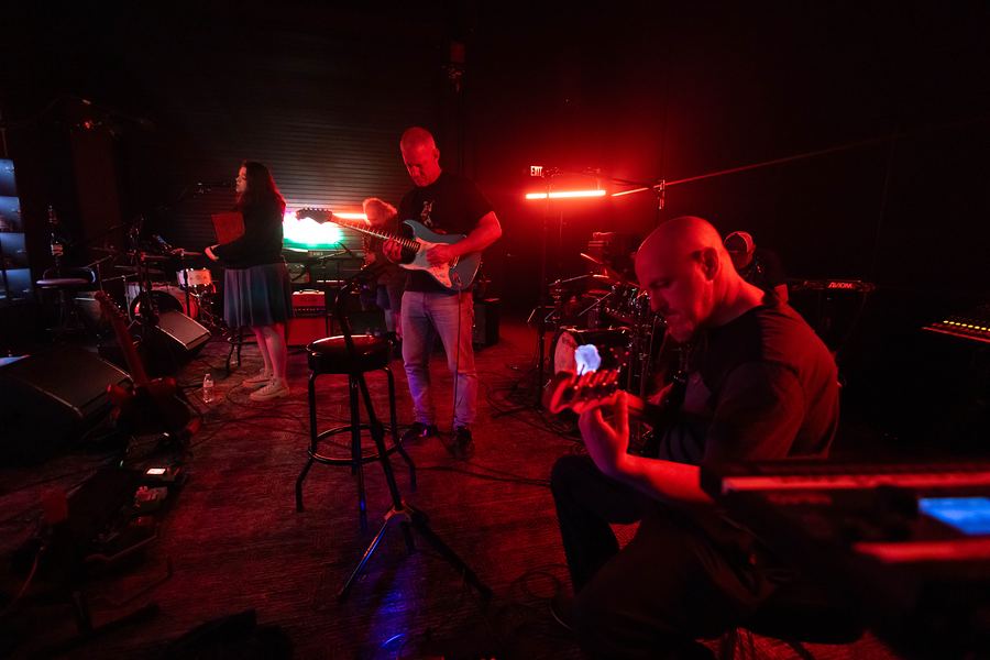 Band rehearsing under red light, with a bassist in the foreground