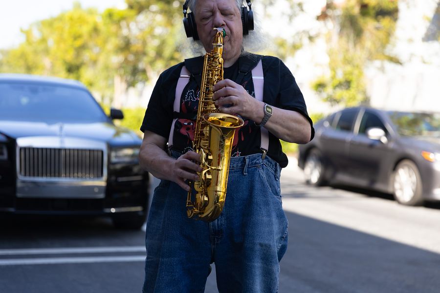 Saxophonist in headphones playing a gold alto sax outdoors beside a black Rolls-Royce