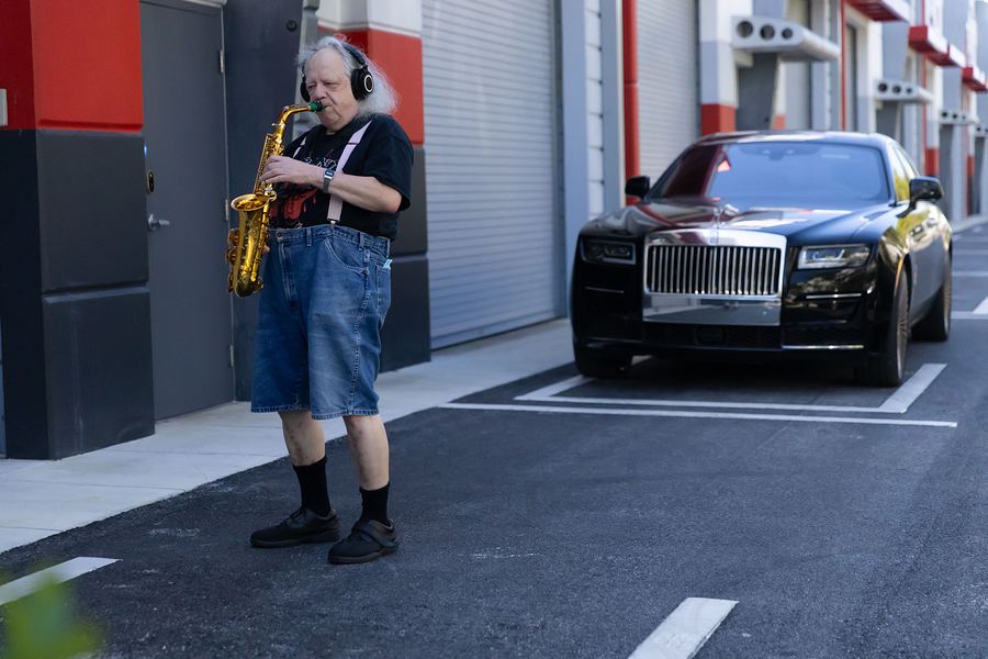 Saxophonist playing on the street next to a parked Rolls-Royce