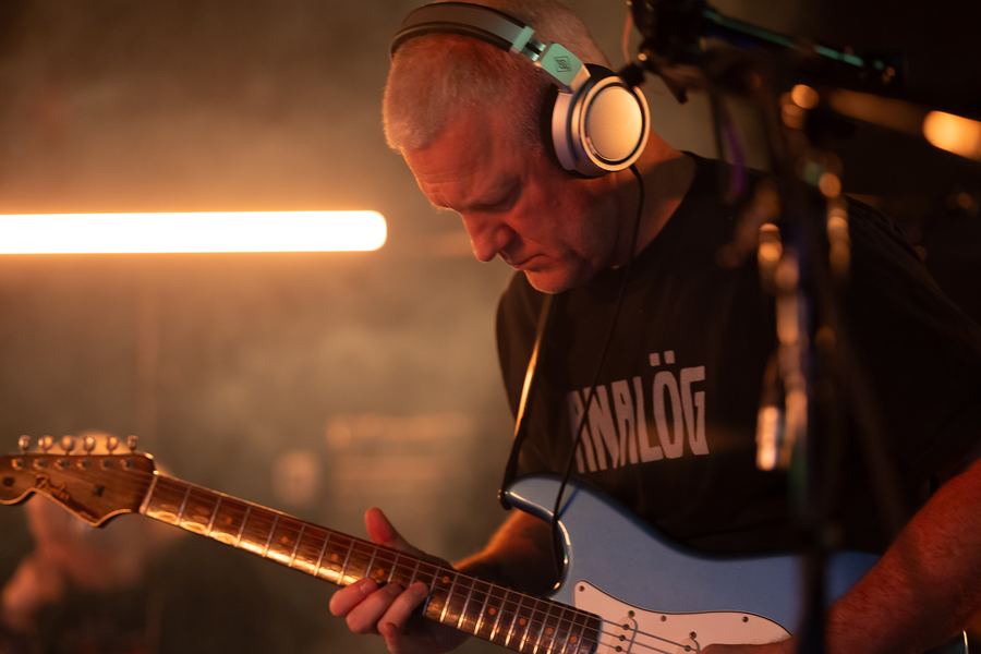 Guitarist in headphones playing a light-blue Stratocaster in warm, hazy light