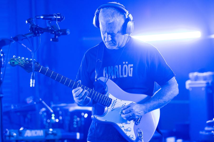 Guitarist in headphones playing a Stratocaster under bright blue light