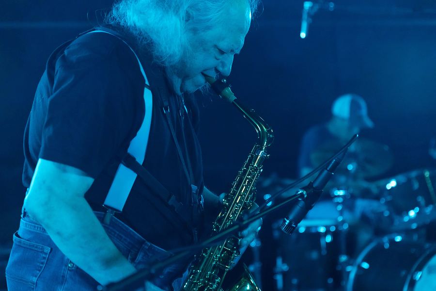 Saxophonist playing under blue light, the drummer behind him