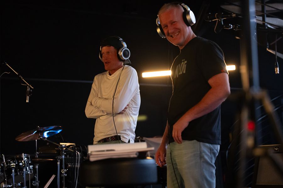Two band members in headphones sharing a laugh in the studio