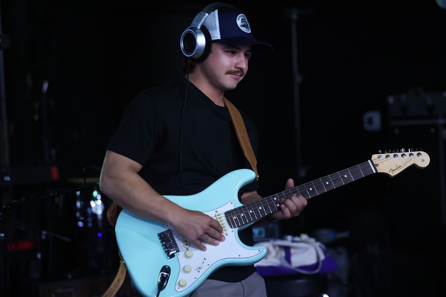 Guitarist in headphones and a cap playing a seafoam-green Fender Stratocaster